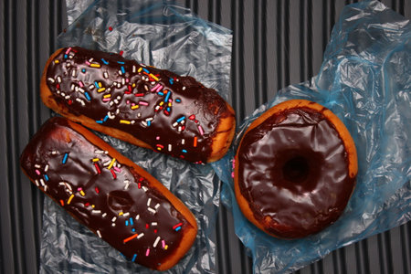 Chocolate donuts and chocolate donut bars topped with multicolored sugar flakes. Placed on a gray...