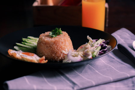 Fried rice, fried egg, cucumber, sliced tomato, green salad and Fried chicken placed on a black plate as a garnish.We call in thai "kao pad American"の写真素材