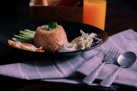 Fried rice, fried egg, cucumber, sliced tomato, green salad and Fried chicken placed on a black plate as a garnish.We call in thai "kao pad American"の写真素材
