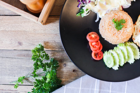 Fried rice, fried egg, cucumber, sliced tomato, green salad and Fried chicken placed on a black plate as a garnish.We call in thai "kao pad American"の写真素材