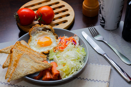 Breakfast, fried eggs, fried sausage, vegetable salad and toast on a brown wooden table with coffee...