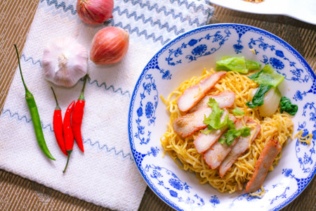Egg Noodles with Barbeque Pork in Chinese Style Plates on a Wooden Table with Tea and 
garnish in thailand.の写真素材