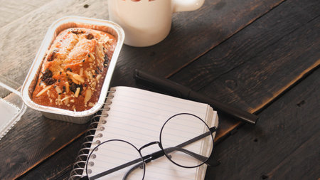 Banana Cake on a black wooden table With note book, glasses, and coffee mugs.の写真素材