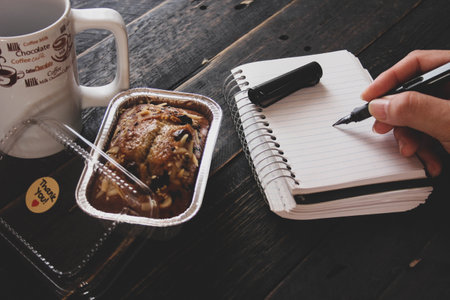 Banana Cake on a black wooden table With note book, glasses, and coffee mugs.の写真素材