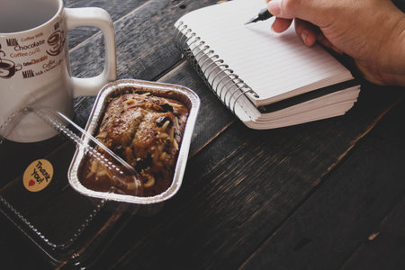 Banana Cake on a black wooden table With note book, glasses, and coffee mugs.の写真素材