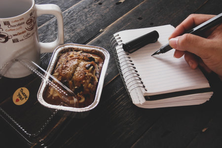 Banana Cake on a black wooden table With note book, glasses, and coffee mugs.