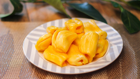 Jackfruit is fresh in a white plate, placed on a wooden table with jackfruit branches in thailand.