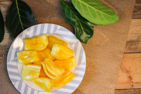 Jackfruit is fresh in a white plate, placed on a wooden table with jackfruit branches in thailand.