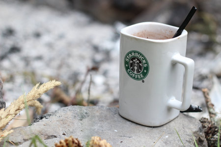Washington, USA - January 13 2023 : Starbucks Coffee Mug Placed on rocks around a camping campfire with pine cones and reeds, modern tones.のeditorial素材