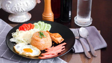 Fried rice, fried egg, cucumber, sliced tomato, green salad and Fried chicken placed on a black plate as a garnish.の写真素材