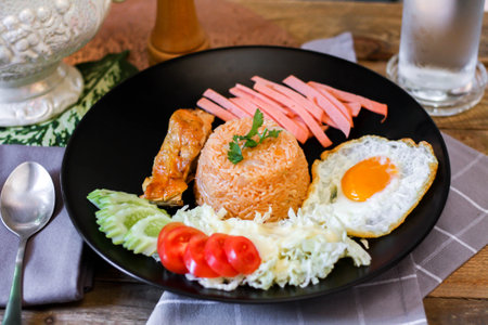 Fried rice, fried egg, cucumber, sliced tomato, green salad and Fried chicken placed on a black plate as a garnish.の写真素材