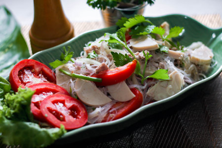 Spicy vietnamese sausages salad placed in a leaf-shaped green plate. With onion, garlic, red pepper on a black wooden table in thailand.の写真素材