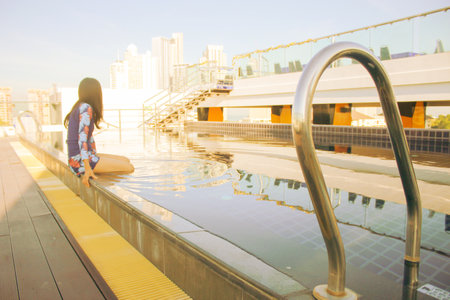 Young Asian woman sitting in a swimming pool on a hot day. Image in warm colors, global warming, hot weather, swimming pool on a hot day.の写真素材