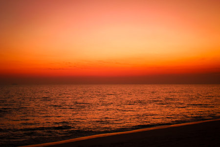 The sea after sunset has an orange glow and an orange sky with no clouds.の写真素材
