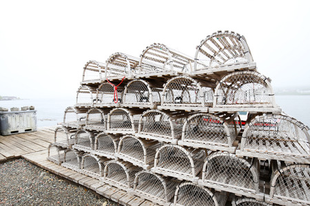 On a foggy day. Old style wooden lobster traps neatly piled at a Nova Scotia fishing village around Louisbourg, Nova Scotia, Canada.の写真素材