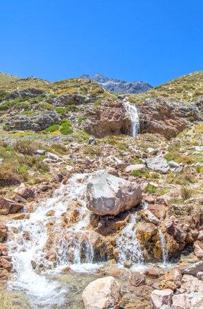 Cascading Waterfall at El Yeso, Cajon del Maipo, Chile. It is a reservoir located in the Andes, in the Santiago Metropolitan Region. Majestic Mountain top in the backgroundの写真素材