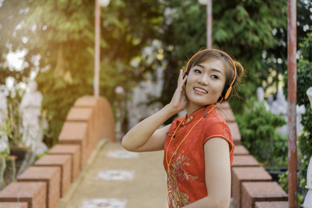 Beautiful Asian girl wearing Cheongsam red dress listening to music be happy. the celebration of something in a joyful and exuberant way. select focusの写真素材