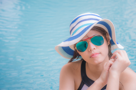 Beautiful girl in swimming pool. She has beautiful skin. She wears blue glasses. And white, blue and blue striped hats.の写真素材