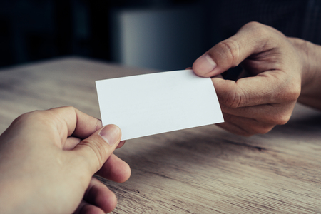 Two businessmen exchanged business cards on a wooden table. White business cards. Copy space.の写真素材