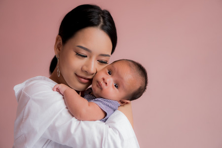 Beautiful Asian mother Kiss and cuddle in the bedroom. Pink background.