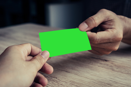 Two businessmen exchanged business cards on a wooden table. Green screen business cards. Copy space. Vintage Style. Business Concepts.の写真素材