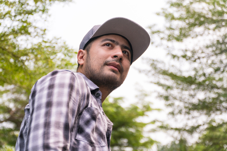 Portrait Handsome man : Good looking young man. He has a beard and wears a hat. He has an interesting smile. Looking for someone. Behind him, full of green trees. Copy space.の写真素材