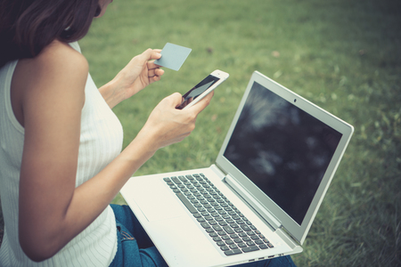 Beautiful girl is shopping through a laptop in the park. She bought online through the card. She is very happy. Vintage style. Copy space.の写真素材