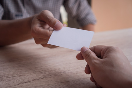 Two businessmen exchanged business cards on a wooden table. Introduction and Exchange of Connections. White business cards. Copy space.の写真素材