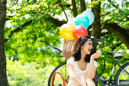 Portrait Asian women in the park. She was sitting happily laughing. In the back, she has a variety of craft and balloons. select focus. Copy space. Tree background.の写真素材