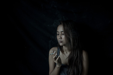 Depressed Asian beautiful woman smoking. She is thinking her future life and feel stressed, Health care for World No Tobacco Day on 31 May every year. copy space. Black background.の写真素材