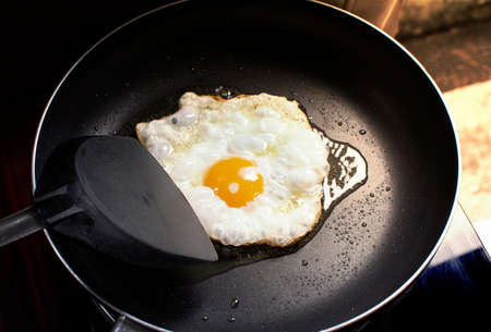 Fried sunny side up egg in a black hot pan and plastic spade at kitchen in home.
