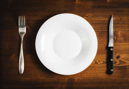 White empty plate with a fork and knife on a wooden table.の写真素材