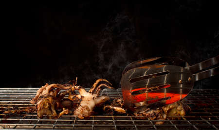 Grilled octopus on a metal grill with food tongs and a black background.の写真素材