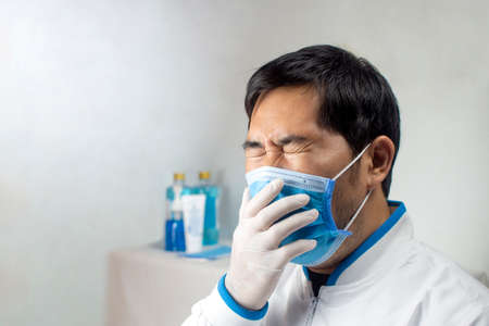 The Doctor coughing in a medical mask at a white room of hospital.の写真素材