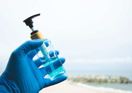 Hand gel sanitizer in hand with blue gloves on the beach blurred backgroundの写真素材