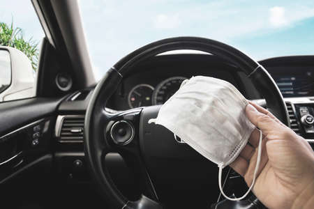Medical face mask holding on driver hand inside to the car , Coronavirus (COVID-19) prevention...