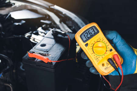 Mechanic checking car battery voltage with digital multimeter