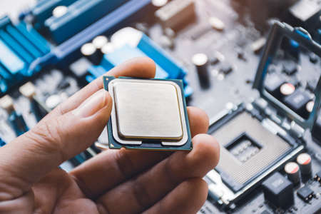 CPU processor chip in technician hand and computer motherboard background