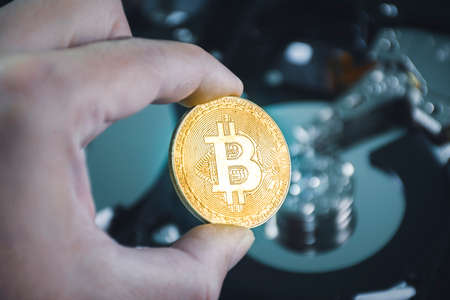Close up of gold bitcoin in the hand with hard disk platters blurred on backgroundの写真素材