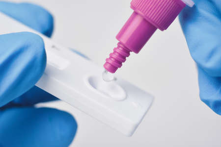 Hand placing the secretions sample into the SARS CoV-2 Rapid antigen test kit (ATK) with the extraction tubeの写真素材