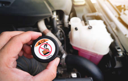 A mechanic hand is clutching a radiator cap with a high temperature dangerous warning notice.の写真素材