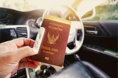 Tourist hand holding Thailand passport, credit card, covid-19 negative test tape on a hand in the car interior with a sunlightの写真素材