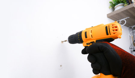 The mechanic uses an electric screwdriver or an electric drill to secure the nut to the white wall...
