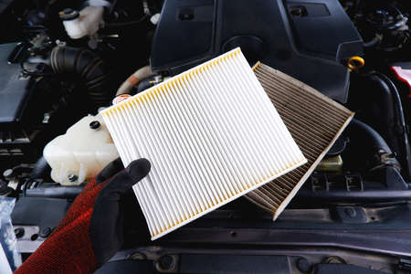 New air filter in a hand and old filthy filter placed on the car engine compartment, Automobile...