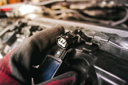 The auto mechanic is unplugging the ignition coil of the car engine in the engine compartment.の写真素材
