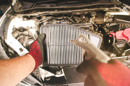 Car air filter in auto mechanic hand is blowing dust and cleaning with air blow gunの写真素材
