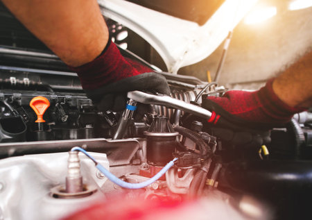 The red gloved hand of the auto mechanic is fastening the bolt with the socket wrench to fix the vehicle engine.の写真素材