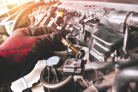 A auto mechanic is installing automobile iridium spark plugs into the ignition socket of the engine block in the engine compartment.の写真素材