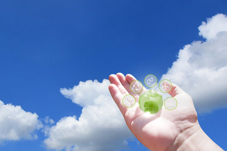 Hand holding green globe with eco energy icon on blue sky with white clouds background, Clean energy conceptの写真素材