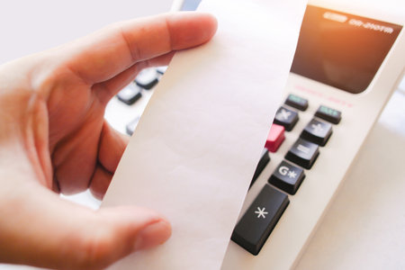 Hand holding blank white paper slip with printing calculator on table, Close up a white paper slip...